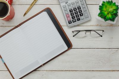 Image of calculator, glasses and notepad.