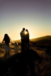 Family watching sunset on hill.